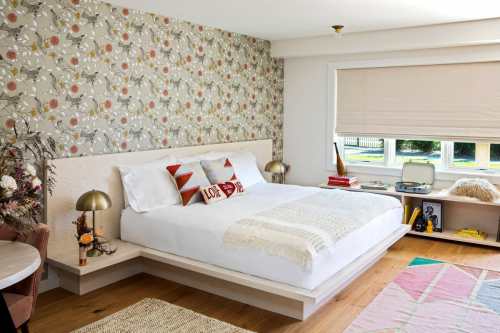 A modern bedroom featuring a floral accent wall, a white bed with decorative pillows, and stylish lighting.