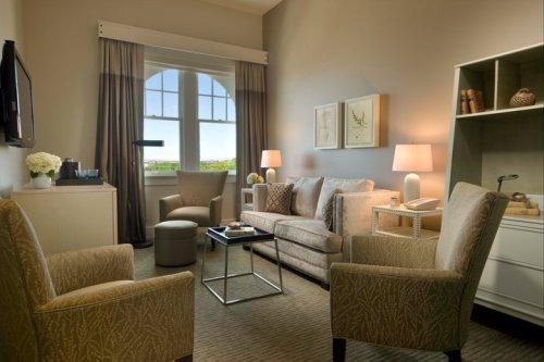 Cozy hotel room with a sofa, two chairs, a coffee table, and large windows offering a view. Soft lighting and decor.