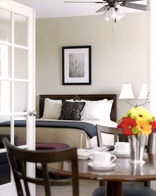 Cozy bedroom with a bed, framed artwork, and a dining area featuring a table with flowers and tableware.
