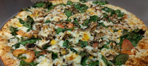 A close-up of a pizza topped with spinach, mushrooms, tomatoes, and melted cheese on a golden crust.