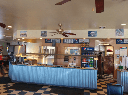 Interior of a casual restaurant featuring a counter, menu boards, and a soda fountain, with checkered flooring.