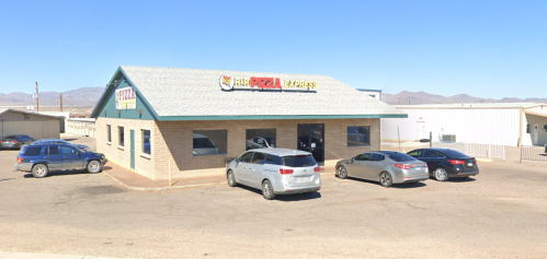 A brick building with a sign reading "Pizza" and several cars parked outside under a clear blue sky.