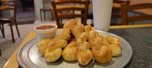 A plate of golden-brown twisted breadsticks with a side of marinara sauce, set on a table in a casual dining space.