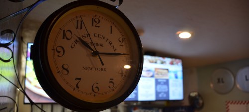 A vintage clock displaying the time, labeled "Grand Central Terminal, New York," with a blurred background of screens.