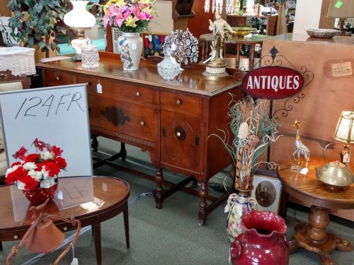 A vintage wooden sideboard surrounded by various antiques, including vases, lamps, and decorative items.