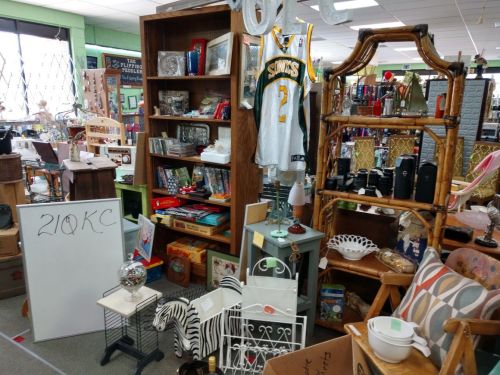 A cluttered thrift store display featuring furniture, decor, a sports jersey, and various collectibles.