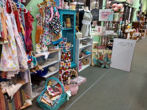 A colorful display of vintage items, including dresses, decor, and crafts, in a charming shop setting.