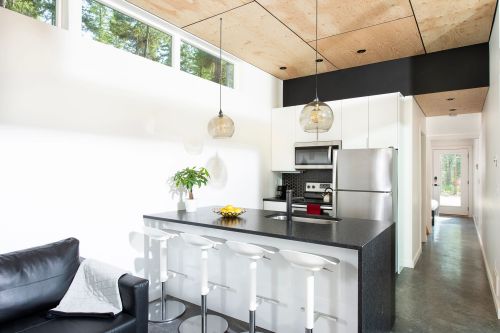 Modern kitchen with a black countertop, white cabinets, pendant lights, and a cozy seating area. Bright and airy design.