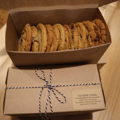 A box of warm cookies, neatly arranged and tied with string, sits on a wooden surface.