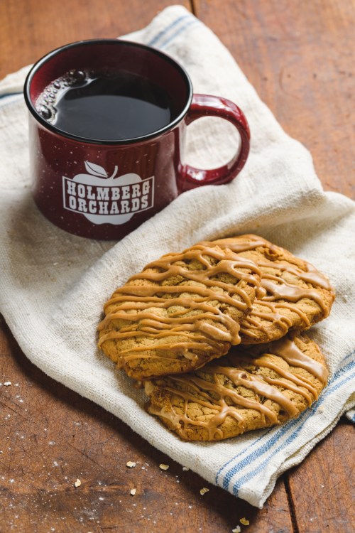 A cup of coffee beside two drizzled cookies on a linen cloth, set on a wooden table.