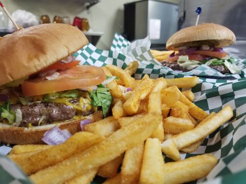 A close-up of a cheeseburger with lettuce, tomato, and onion, served with a side of golden fries in a checkered basket.