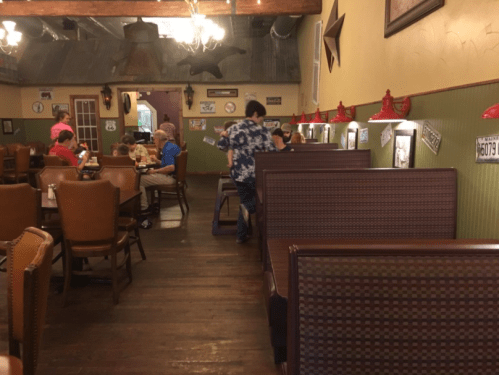 A cozy restaurant interior with wooden floors, booths, and diners enjoying their meals. Decor includes vintage signs.