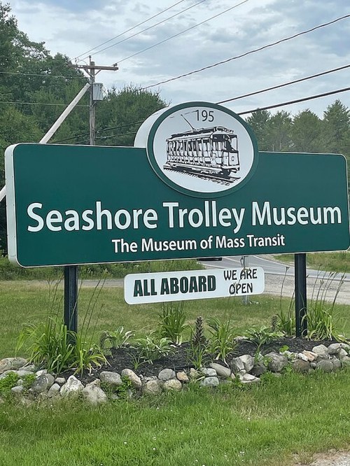 Sign for the Seashore Trolley Museum, featuring a trolley graphic and the text "ALL ABOARD WE ARE OPEN."