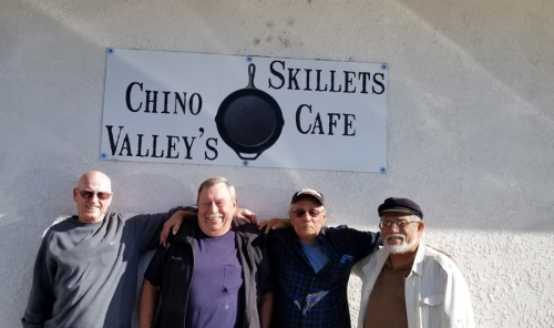 Four men stand together in front of a sign for "Chino Valley's Skillets Cafe."
