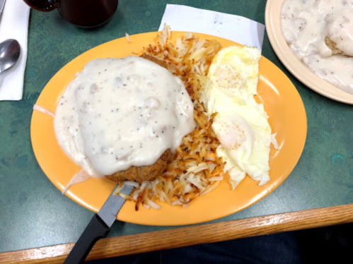 A plate of chicken fried steak topped with gravy, served with hash browns and two eggs.