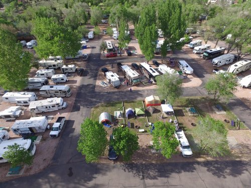Aerial view of a busy RV park with numerous campers, tents, and green trees in a scenic outdoor setting.