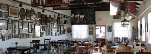 Cozy restaurant interior with wooden chairs, tables, and walls adorned with various framed pictures and artwork.