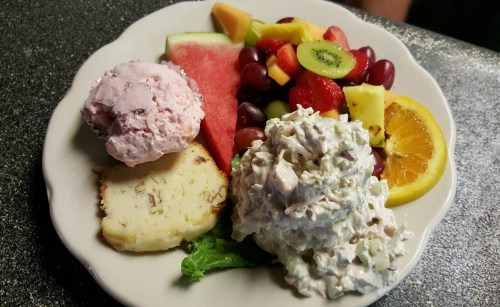 A plate with two scoops of ice cream, a fruit salad, and a scoop of chicken salad on lettuce, garnished with orange.