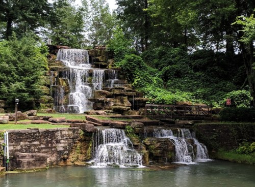 A serene waterfall cascading over rocks, surrounded by lush greenery and a calm pond at the base.