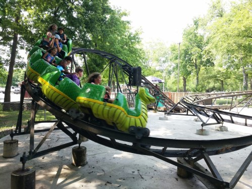 A colorful roller coaster with children enjoying a ride through a park on a sunny day.