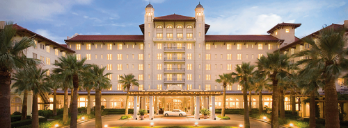 A grand hotel with a lighted facade, palm trees in the foreground, and a welcoming entrance at dusk.