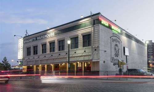 Exterior of Spaghetti Warehouse restaurant at dusk, featuring neon signs and a classic architectural design.