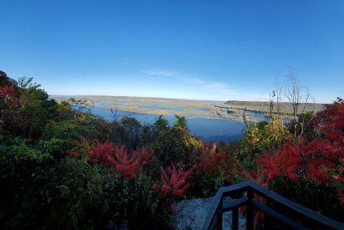 A scenic view of a lake surrounded by colorful autumn foliage under a clear blue sky.