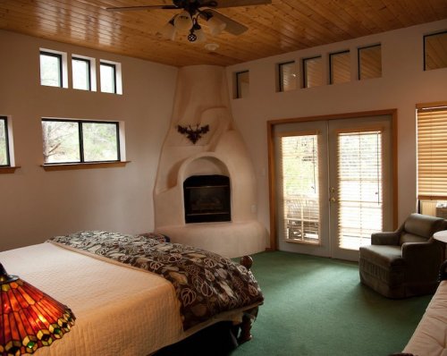 Cozy bedroom with a fireplace, large windows, and a green carpet, featuring a bed and a comfortable chair.