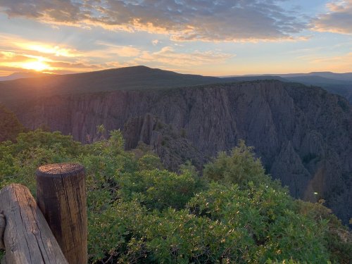 Sunset over a dramatic canyon landscape, with lush greenery in the foreground and colorful clouds in the sky.