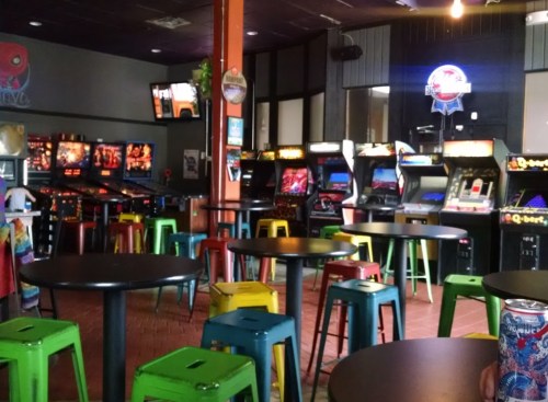A vibrant arcade with colorful stools, pinball machines, and classic arcade games in a lively setting.