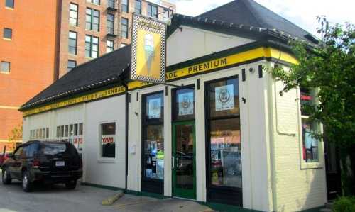 A charming ice cream shop with a colorful sign, featuring large windows and a black SUV parked outside.