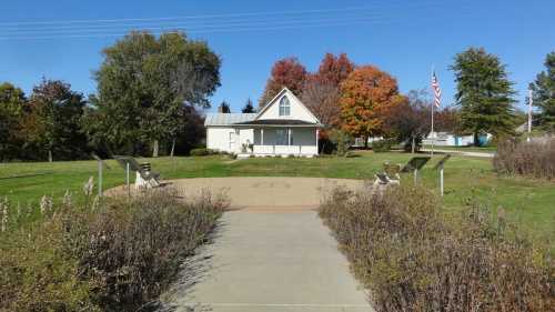 A small white house surrounded by colorful trees and a grassy area, with a path leading to it.