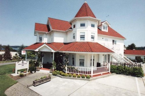 A charming white house with a red roof and turret, featuring a porch and landscaped garden.