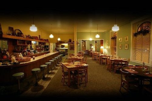 Cozy restaurant interior with wooden tables, bar stools, and warm lighting, creating an inviting atmosphere.