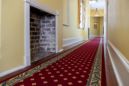 A long hallway with yellow walls, a patterned red carpet, and a brick fireplace on the left side.