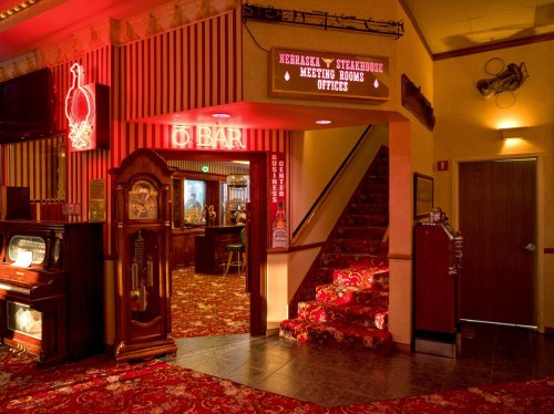 Interior of a restaurant with a bar, staircase, and vintage decor, featuring red and gold accents and neon signs.