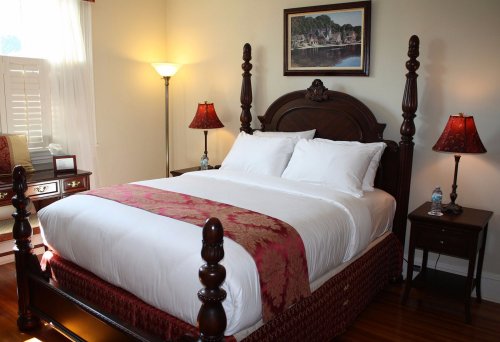 Cozy bedroom featuring a wooden bed with white linens, bedside lamps, and a framed landscape painting on the wall.