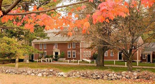 A red-brick building surrounded by trees with autumn leaves, set against a stone wall in a serene landscape.