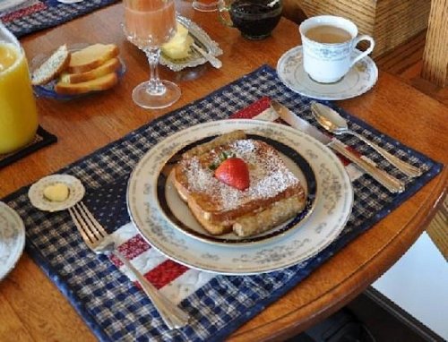 A beautifully set breakfast table featuring French toast with a strawberry, orange juice, and coffee.