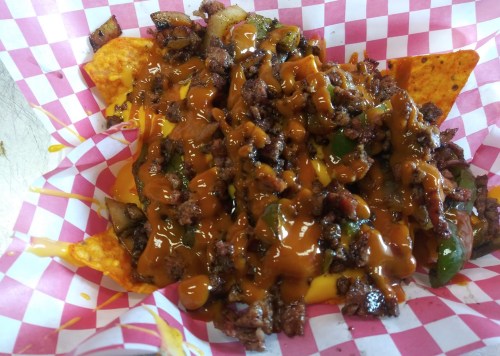 A plate of nachos topped with seasoned beef, melted cheese, and green peppers on a checkered paper background.