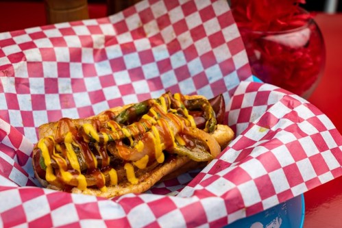 A hot dog topped with grilled onions and mustard, served in a red and white checkered basket.