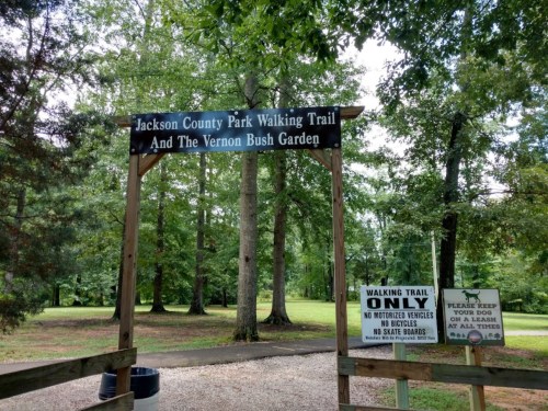 Sign at the entrance of Jackson County Park Walking Trail and Vernon Bush Garden, surrounded by trees.