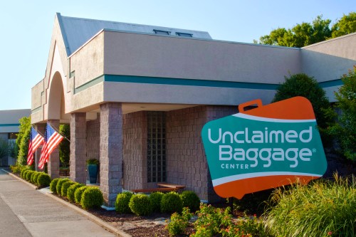 Exterior of the Unclaimed Baggage Center with American flags and greenery in front.