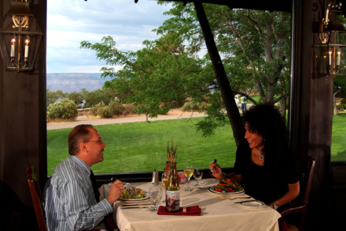 A couple enjoys a meal together at a cozy restaurant with a scenic view of greenery outside.