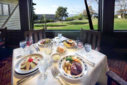 A beautifully set dining table with gourmet dishes and drinks, overlooking a scenic outdoor view.