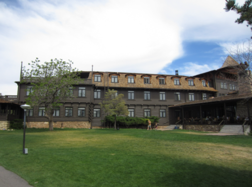 Historic wooden building with multiple windows, surrounded by green grass and trees under a partly cloudy sky.