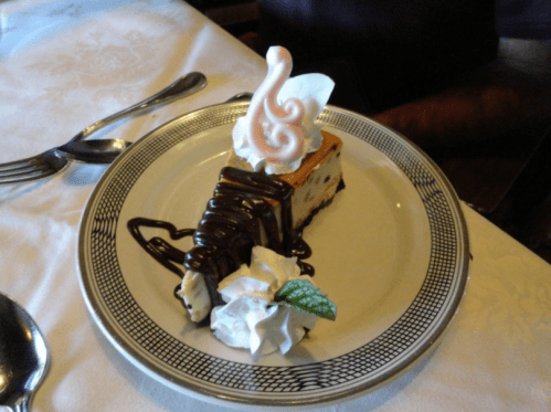 A slice of dessert topped with chocolate sauce, whipped cream, and a decorative swan made of meringue on a plate.