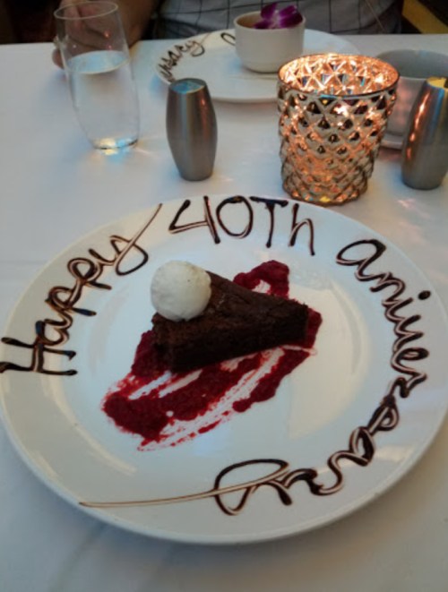 A dessert plate with a chocolate cake slice, raspberry sauce, and a scoop of ice cream, decorated with "Happy 40th Anniversary."