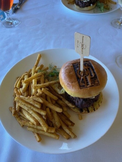 A gourmet burger with a wooden flag on a plate, accompanied by a side of crispy French fries.