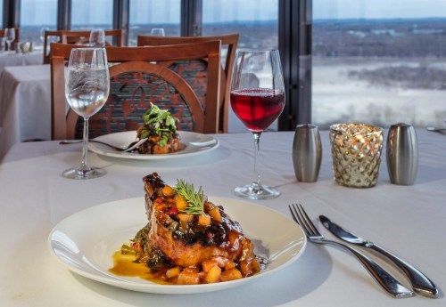 A beautifully plated dish with a glazed meat, accompanied by a salad, wine, and a candle on a dining table with a view.